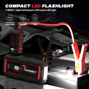 Rooboost compact jump starter with it's flash light shown the attached red jumper cable and clamps connected to a car battery.